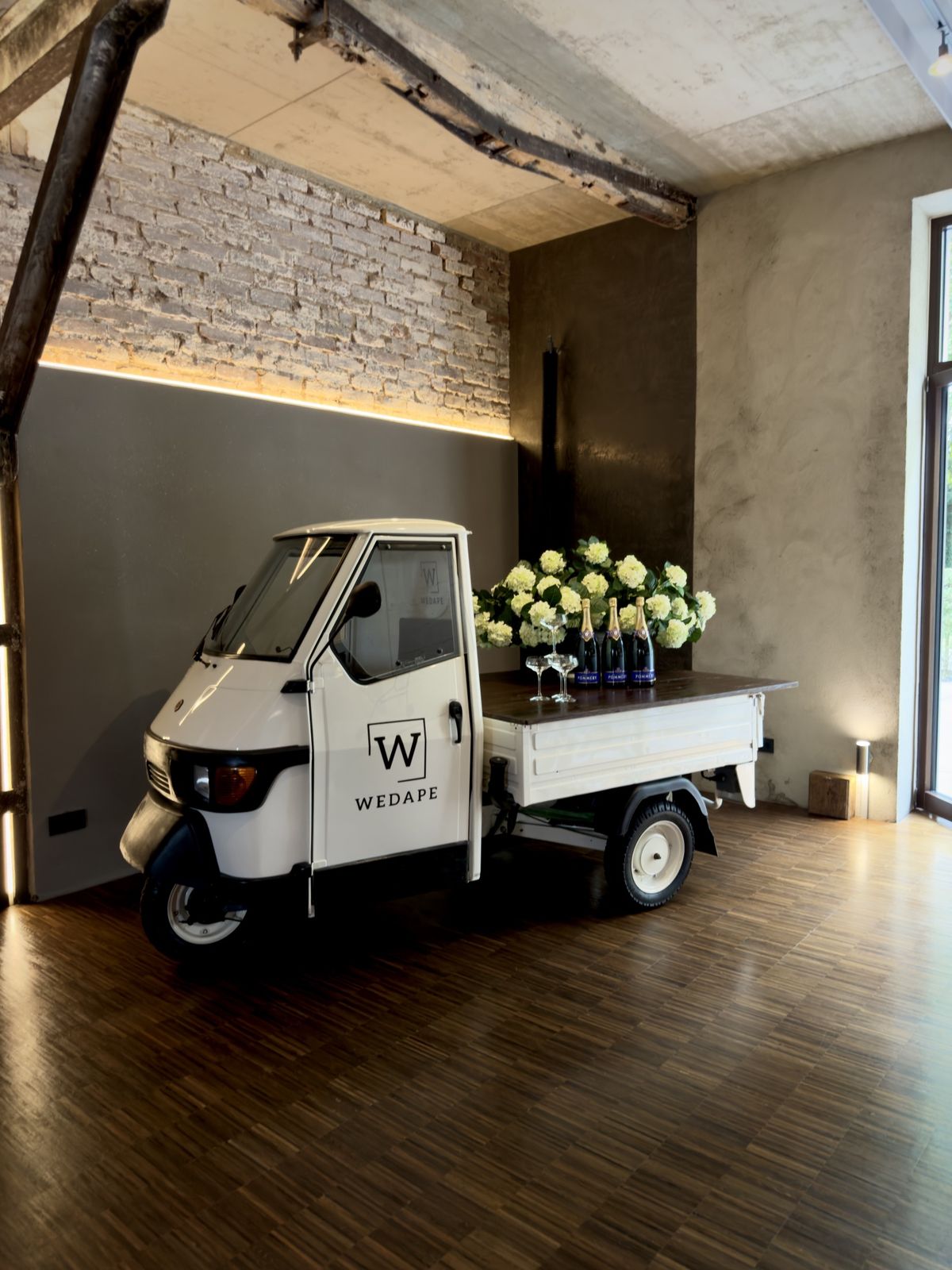Die Piaggio Ape von Wedape mit Sekt und Hortensien in einer Eventlocation